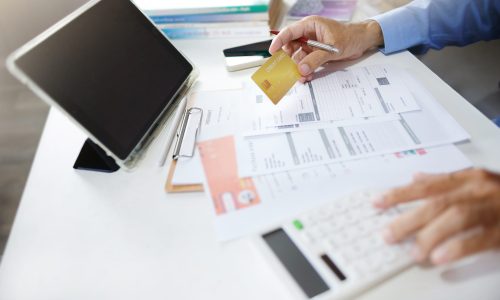 Asian businessman using tablet work on desk holding credit card and checking receipt, documents related to business operations calculate expenses paid via credit card before finalizing the account
